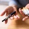 personne tenant des cigarettes dans une main et une e-cigarette dans l'autre main