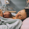 femme sur un lit d'hôpital, allongée, tenant le bébé qu'elle vient d'accoucher, souriante