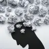silhouette tête baissée, avec des boules de papier au niveau de la tête, signes qu'il y a beaucoup de pensées. Ambiance morose.